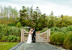 Bride and groom kissing in front of a gate at Plume